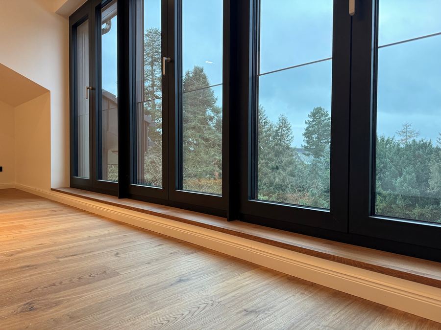 Leerer Wohnraum mit Eichendielen und raumhoher Fensterfront zum Wald