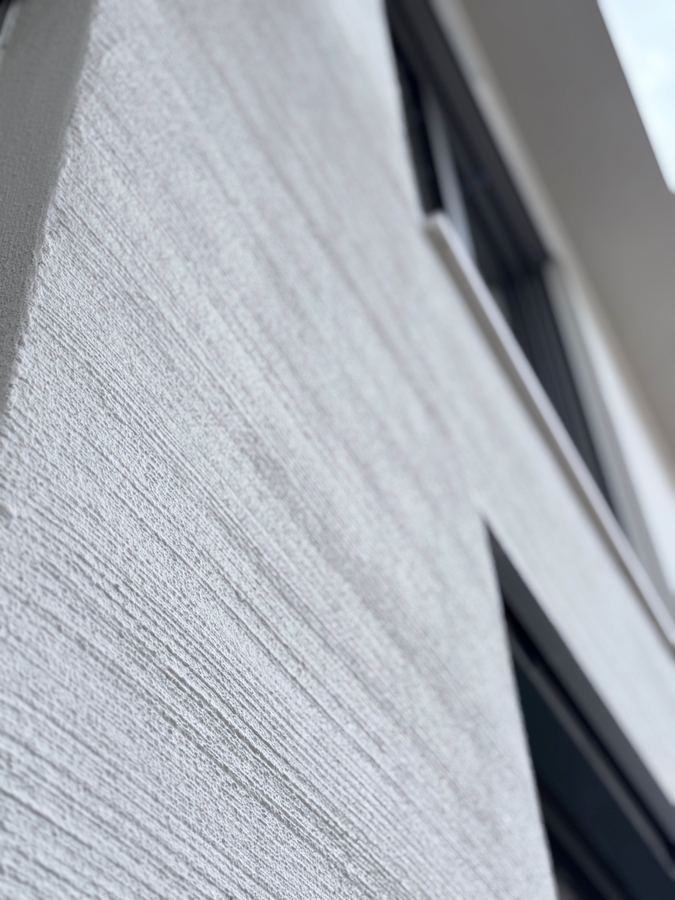 Detail einer besenstrichverputzten Wandfläche neben einem dunklen Fensterrahmen