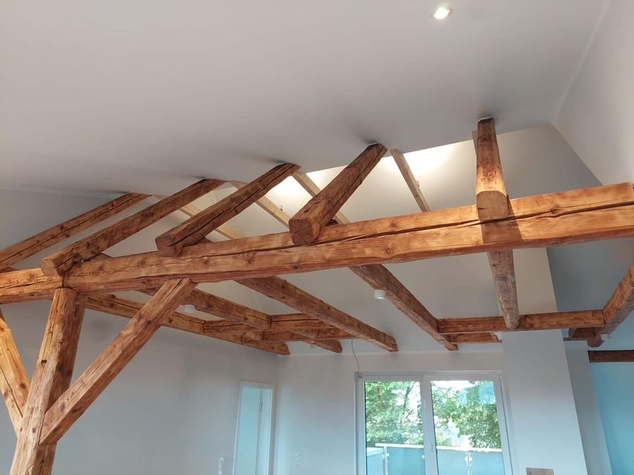 Freigelegtes Dachtragwerk aus Holzbalken über einem weiß gestrichenen Raum