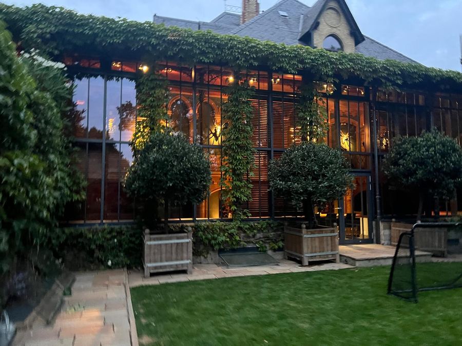 Efeubewachsene Fassade eines Gebäudes am Abend, davor eine Rasenfläche mit Bäumen