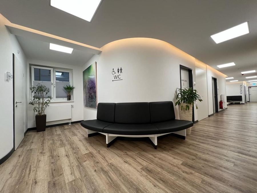 Wartebereich einer Praxis mit Sitzbank, Holzboden und geschwungener Lichtdecke