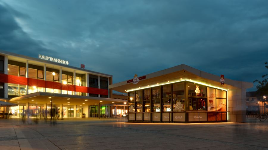 Beleuchtetes Ladengebäude am Abend mit vorgezogenem Vordach