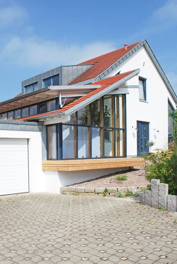 Wohnhaus mit weit heruntergezogenem Dach über dem verglasten Anbau