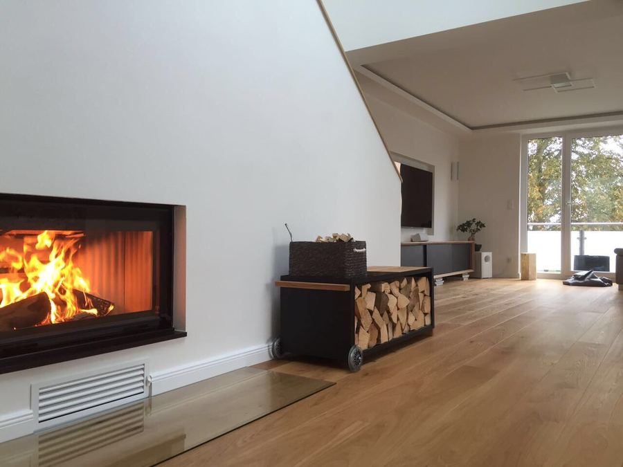 Wohnraum mit Kaminofen, Holzstapel und bodentiefen Fenstern
