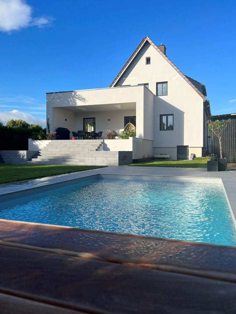 Wohnhaus nach Umbau und Anbau mit Flachdach und überdachter Terrasse, davor ein Pool im Garten