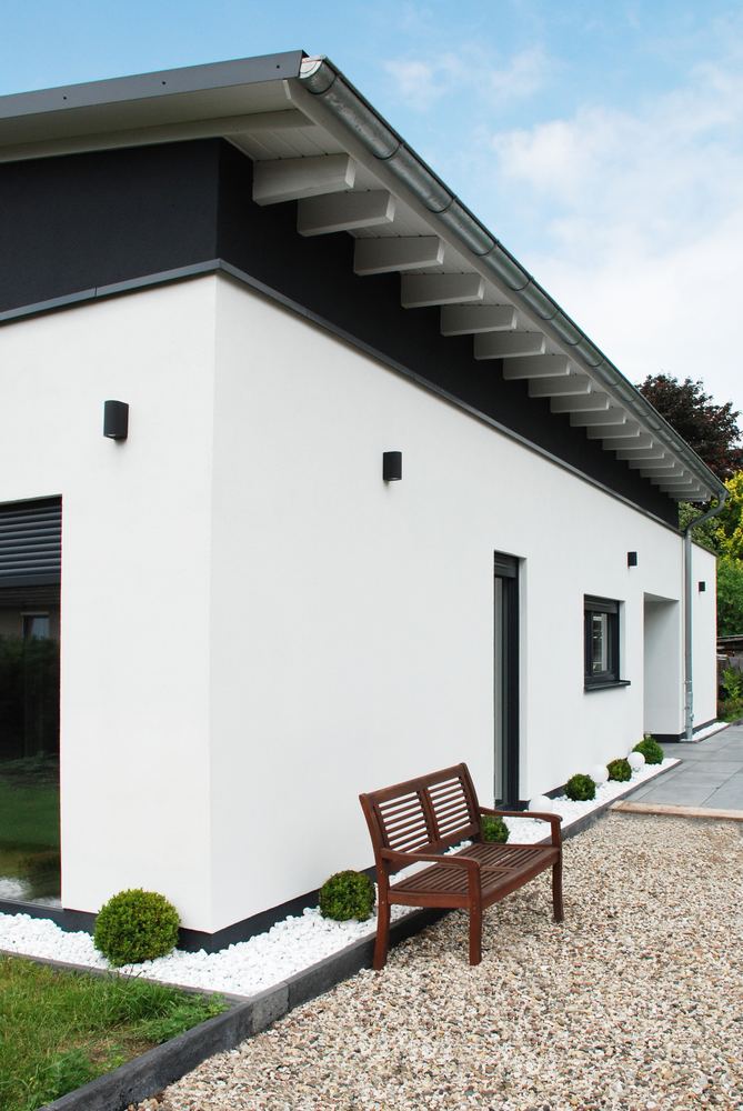 Weißes Wohnhaus mit Pultdach, Kiesstreifen und einer Bank an der Fassade