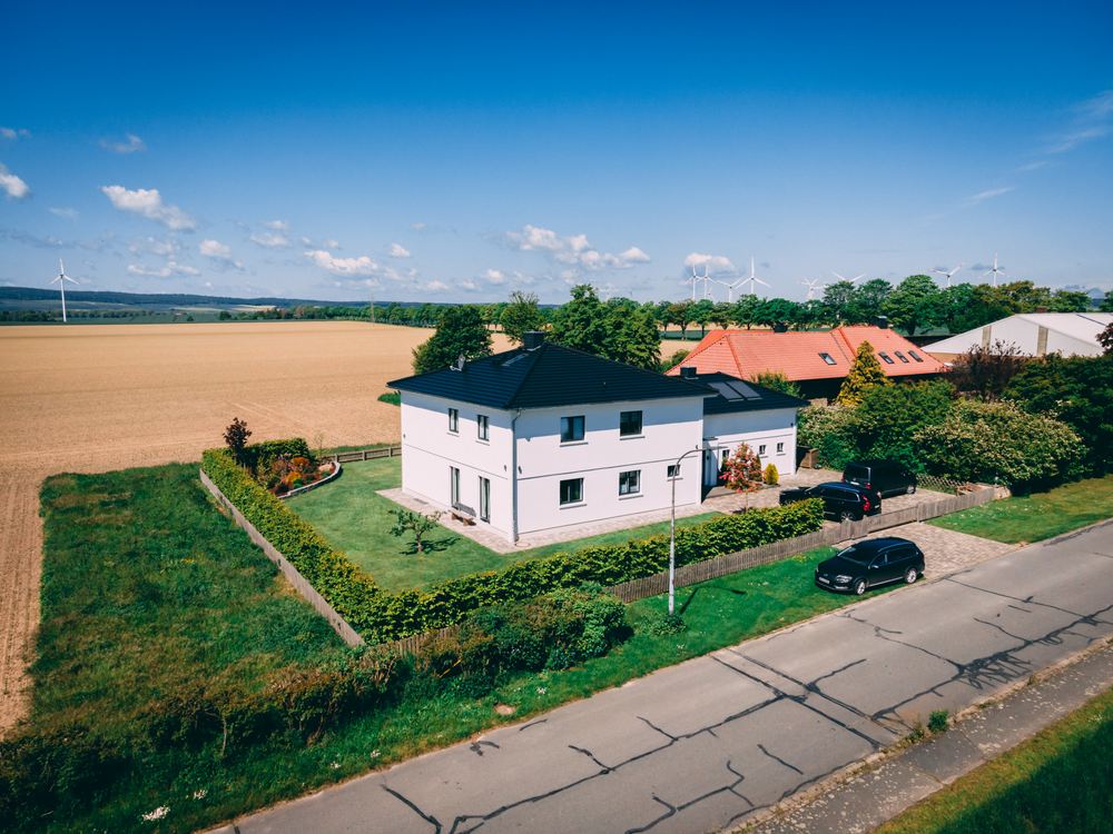 Luftbild eines aufgestockten Einfamilienhauses mit dunklem Walmdach in offener Feldlage