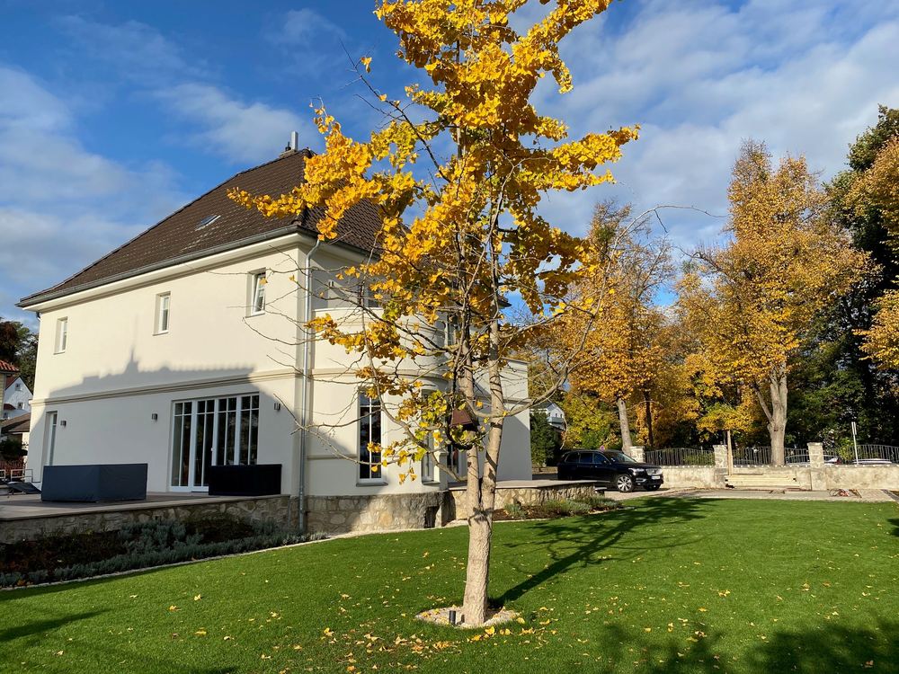 Saniertes Einfamilienhaus mit ausgebautem Dachgeschoss, davor eine Wiese mit herbstlichem Baum