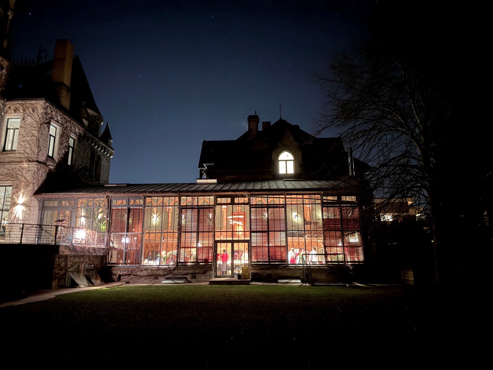 Villa mit angebauter, hell erleuchteter Orangerie bei Nacht